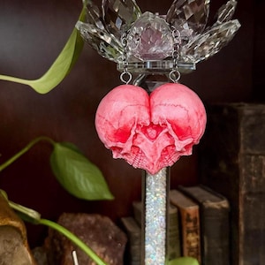 Pink double skull heart sculpture displayed beneath a crystal lotus candle holder with green vine leaves