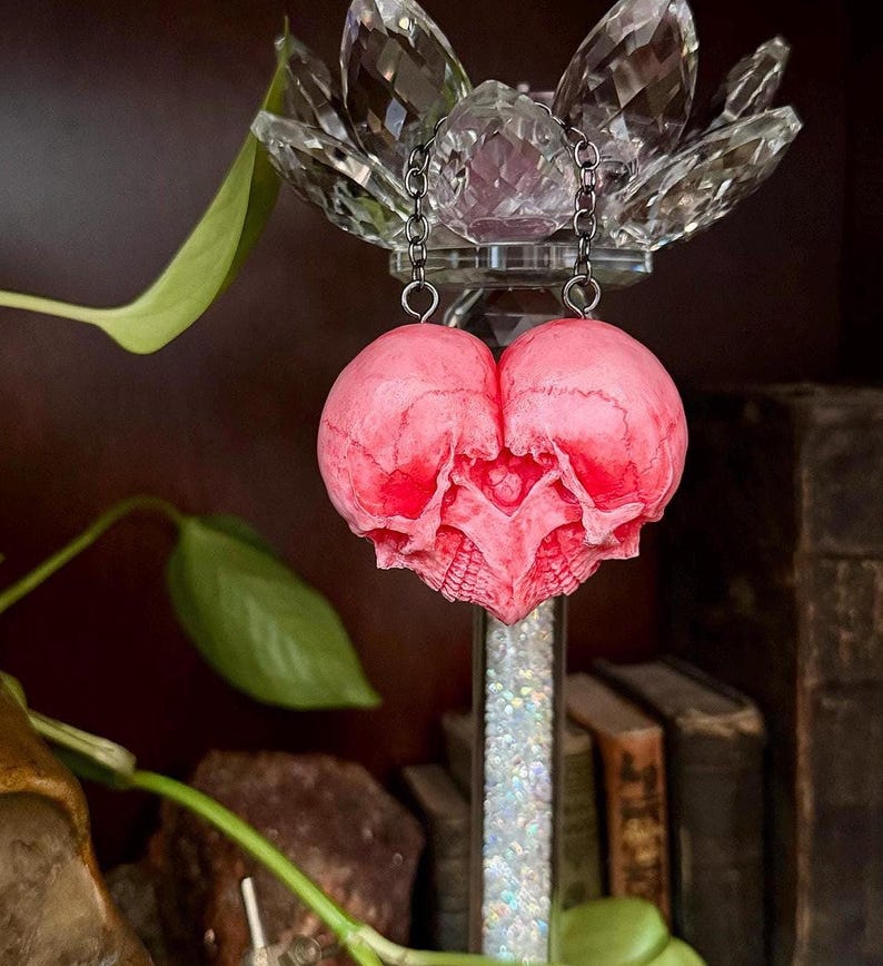 Pink double skull heart sculpture displayed beneath a crystal lotus candle holder with green vine leaves