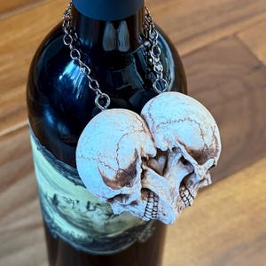 Pale blue-gray double skull heart on a chain around the neck of a wine bottle