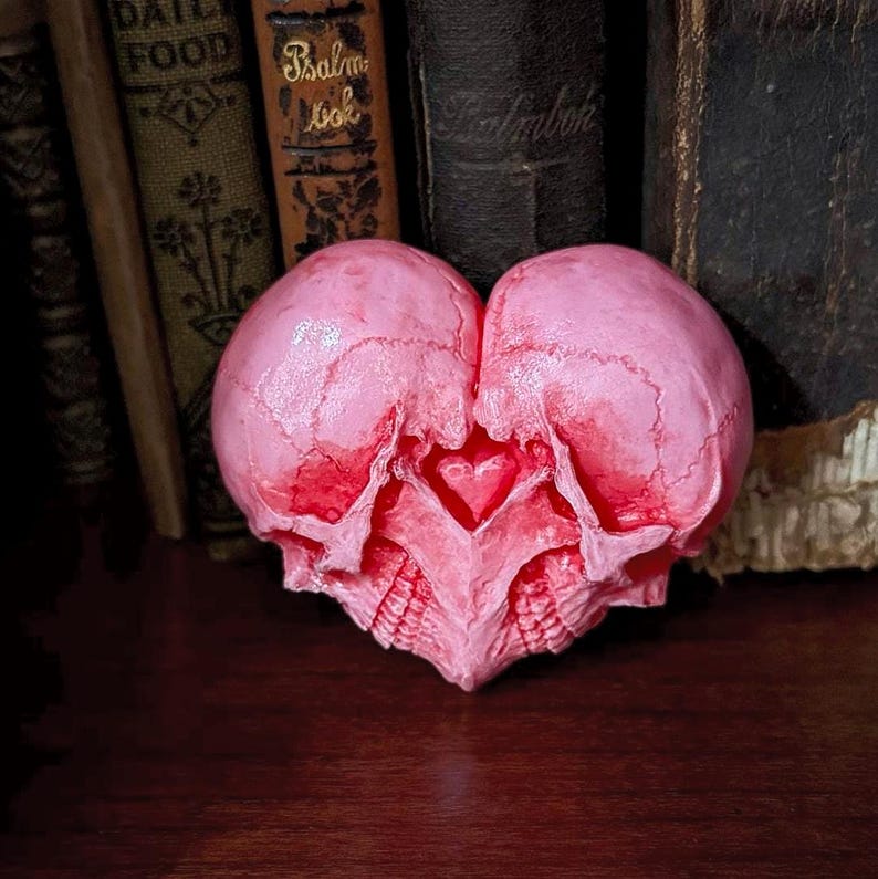 Pink double skull heart sculpture facing forward in front of antique books - two skulls forming a heart shape