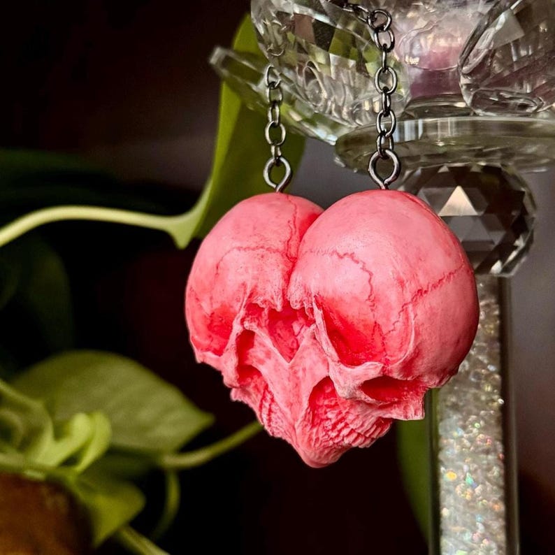 Close-up of a pink double skull heart hanging by two chains from a crystal holder