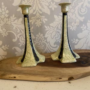 Könnte beinhalten: Ein Paar grüne und schwarze Kerzenhalter aus Keramik mit einer craquelé-Glasur. Die Kerzenhalter sind hoch und schlank mit einem ausgestellten Fuß.