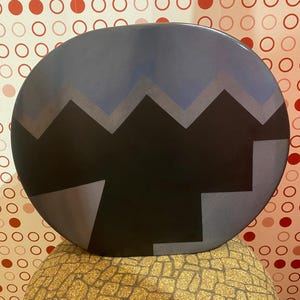 Può includere: Un grande vaso rotondo in ceramica nera con un design geometrico in tonalità di grigio e blu. Il vaso ha una superficie leggermente strutturata.