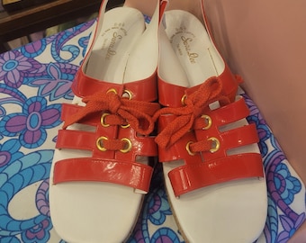 Puede incluir: Un par de sandalias rojas y blancas vintage con un diseño de tiras. Las sandalias tienen punta cuadrada, cordones rojos y ojales dorados. La marca "Sara Lee" es visible en la plantilla blanca.