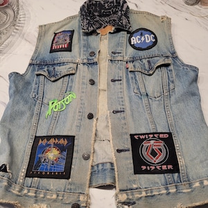 Peut inclure: Un gilet en jean bleu clair avec un col à motifs noir et blanc et plusieurs écussons de groupes, dont AC/DC, Poison, Def Leppard Pyromania et Twisted Sister. Le gilet présente des boutons en métal et des bords effilochés aux emmanchures et à l'ourlet.