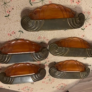 May include: Four vintage cabinet knobs with amber plastic and silver metal accents. The knobs have a decorative, art deco design.