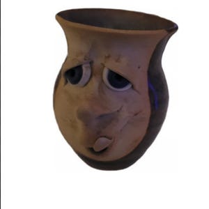 Puede incluir: Una taza pequeña de cerámica marrón con una cara. La taza tiene ojos grandes y redondos, una boca pequeña y una nariz. La taza está esmaltada en un color marrón claro con un esmalte marrón más oscuro en el borde y el asa.
