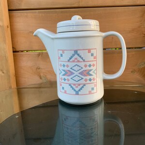 May include: White ceramic coffee pot with a geometric pattern in shades of blue, pink and peach. The pattern is reminiscent of Native American designs.