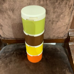 Könnte beinhalten: Ein Satz von vier stapelbaren Behältern mit Deckeln. Die Behälter sind grün, braun, gelb und orange. Die Deckel sind weiß.