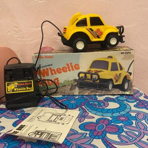 Puede incluir: Un coche de juguete teledirigido amarillo Radio Shack Wheelie Bug con detalles en negro y el número 89. El coche está sobre su caja original, que presenta una imagen del coche. También hay un mando a distancia y una hoja de instrucciones.