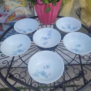 May include: Six white bowls with a blue floral pattern are arranged on a black metal table. The bowls are all the same size and shape, and they have a simple, elegant design.