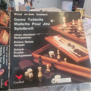 Puede incluir: Un juego de mesa multijuego que incluye ajedrez, damas y backgammon. El juego incluye tableros de juego de madera, piezas de juego, dados y un estuche de transporte. La caja tiene texto en varios idiomas, incluyendo "Game Teblette" y la marca "Cardinal".