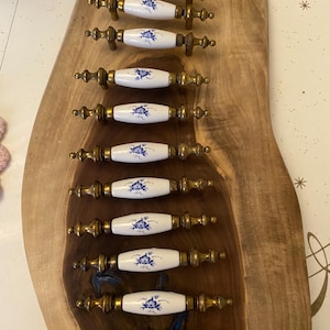 Könnte beinhalten: Zehn antike Schrankknöpfe mit weißen Keramikgriffen und goldenen Metallsockeln. Die Griffe haben ein blaues Blumenmuster.