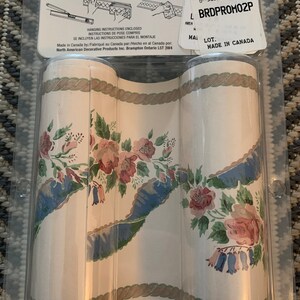 May include: Two rolls of floral wallpaper border with a rope design. The border features a white background with blue, green, and pink flowers. The packaging includes instructions for hanging the border.