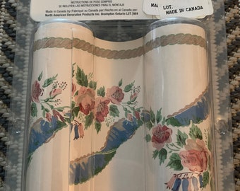 Puede incluir: Dos rollos de cenefa de papel tapiz floral con un diseño de cuerda. La cenefa presenta un fondo blanco con flores azules, verdes y rosas. El paquete incluye instrucciones para colgar la cenefa.