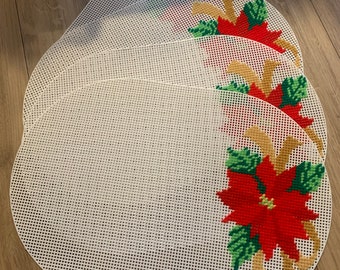 May include: Four white oval-shaped placemats with a red poinsettia and gold ribbon design. The placemats are made of a canvas-like material.