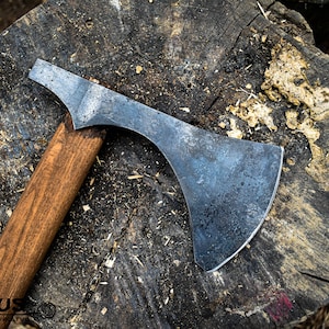 Könnte beinhalten: Eine handgeschmiedete Axt mit einem Holzstiel und einem dunkelgrauen Metallkopf. Die Axt liegt auf einem Baumstumpf.