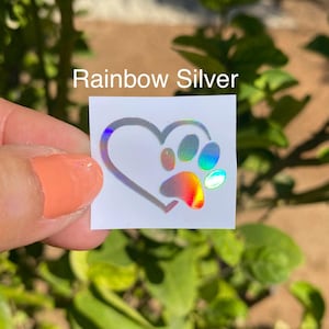 May include: A rainbow silver vinyl sticker with a paw print inside a heart. The sticker is on a white background.
