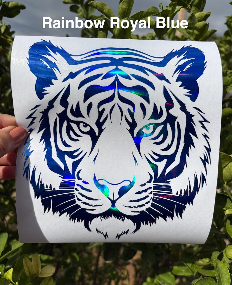 May include: A decal featuring a tiger head graphic with a holographic rainbow royal blue finish on a white backing. The design displays intricate black and blue striped patterns and the text Rainbow Royal Blue at the top of the sheet.