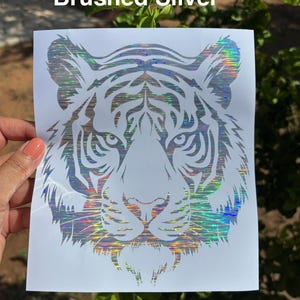 May include: A decal featuring a stylized tiger head design with a holographic, brushed silver finish. The tiger graphic is printed on a white rectangular backing sheet. The text "Brushed Silver" is visible at the top of the image.