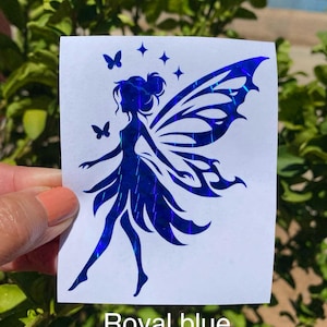 May include: A royal blue holographic decal on a white backing featuring a silhouette of a fairy with large wings, two small butterflies, and three four-pointed stars. The text "Royal blue moisac" is printed at the bottom of the decal.