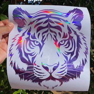 May include: A decal featuring a stylized tiger head graphic with a holographic purple finish on a white backing sheet. The design includes intricate black-toned cutouts for the tiger's facial features and stripes, with the word Purple printed above.