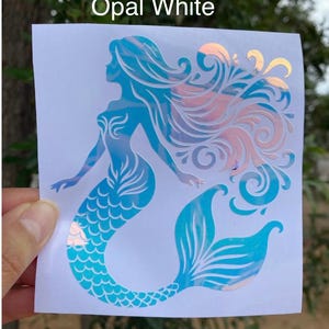 K&ouml;nnte beinhalten: Opal White Meerjungfrau-Aufkleber. Der Aufkleber zeigt eine Meerjungfrau-Silhouette mit flie&szlig;endem Haar und einer Fischschwanzflosse. Das Design enth&auml;lt Blaut&ouml;ne und schillernde Akzente, mit dem Text "Opal White" oben.