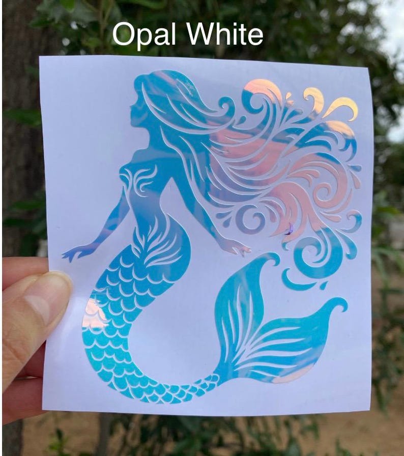K&ouml;nnte beinhalten: Opal White Meerjungfrau-Aufkleber. Der Aufkleber zeigt eine Meerjungfrau-Silhouette mit flie&szlig;endem Haar und einer Fischschwanzflosse. Das Design enth&auml;lt Blaut&ouml;ne und schillernde Akzente, mit dem Text "Opal White" oben.