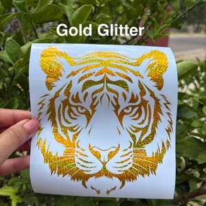 May include: A gold glitter tiger head decal on a white backing sheet with the text Gold Glitter printed above the design. The tiger graphic features intricate cut-out details forming the face, eyes, and whiskers in a shimmering metallic finish.