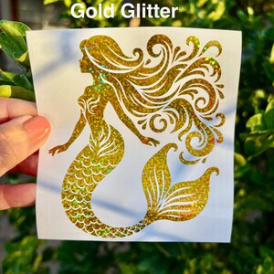 K&ouml;nnte beinhalten: Ein goldener Glitzer-Meerjungfrau-Aufkleber mit flie&szlig;endem Haar und einem detaillierten Schwanz. Der Aufkleber hat einen schimmernden Effekt mit Hauch von Rot, Gr&uuml;n und Gold. Der Text "Gold Glitter" ist oben aufgedruckt.