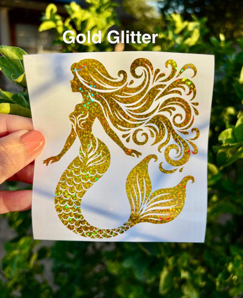 K&ouml;nnte beinhalten: Ein goldener Glitzer-Meerjungfrau-Aufkleber mit flie&szlig;endem Haar und einem detaillierten Schwanz. Der Aufkleber hat einen schimmernden Effekt mit Hauch von Rot, Gr&uuml;n und Gold. Der Text "Gold Glitter" ist oben aufgedruckt.