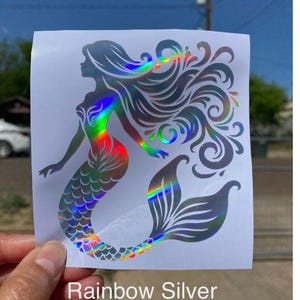 K&ouml;nnte beinhalten: Ein holografischer Meerjungfrau-Aufkleber mit Regenbogeneffekt. Die Meerjungfrau hat flie&szlig;endes Haar und einen detaillierten Schwanz. Der Text "Rainbow Silver" ist unten auf dem Aufkleber aufgedruckt.