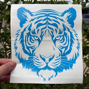 May include: A square white decal featuring a sky blue matte tiger head graphic with intricate facial stripes and whiskers. The text Sky Blue matte is printed in white at the top of the decal. The design is centered on a white backing sheet.