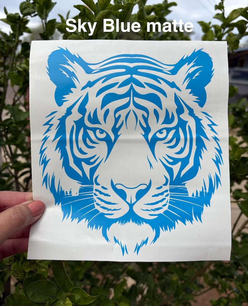 May include: A square white decal featuring a sky blue matte tiger head graphic with intricate facial stripes and whiskers. The text Sky Blue matte is printed in white at the top of the decal. The design is centered on a white backing sheet.