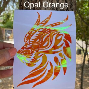 K&ouml;nnte beinhalten: Ein Aufkleber mit einem Drachenkopf in orange und gr&uuml;ner, schillernder Farbe. Der Aufkleber ist auf wei&szlig;em Hintergrund und tr&auml;gt oben die Aufschrift "Opal Orange".