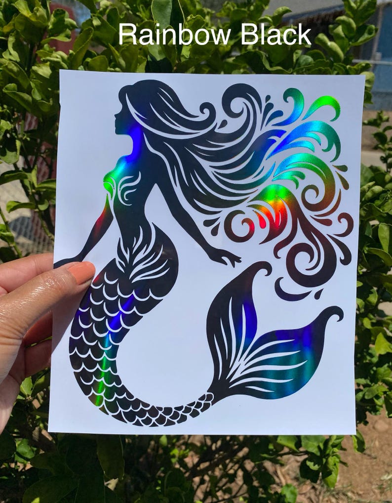 K&ouml;nnte beinhalten: Schwarzer Meerjungfrau-Aufkleber mit holografischen Regenbogenakzenten. Der Aufkleber tr&auml;gt oben den Text "Rainbow Black". Die Meerjungfrau hat lange, flie&szlig;ende Haare und einen detaillierten Schwanz. Der Aufkleber wird von einer Hand gehalten.