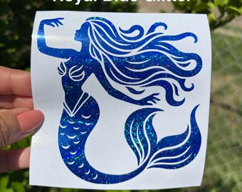 May include: A royal blue glitter decal featuring a silhouette of a mermaid with long flowing hair and a detailed tail. The design is printed on a white square backing. The text Royal Blue Glitter is visible at the top of the image.