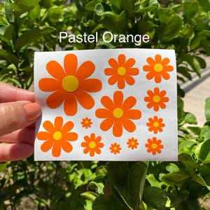 May include: A sheet of pastel orange flower stickers with yellow centers. The sheet contains various sizes of the flower stickers. The text "Pastel Orange" is printed at the top of the sheet.