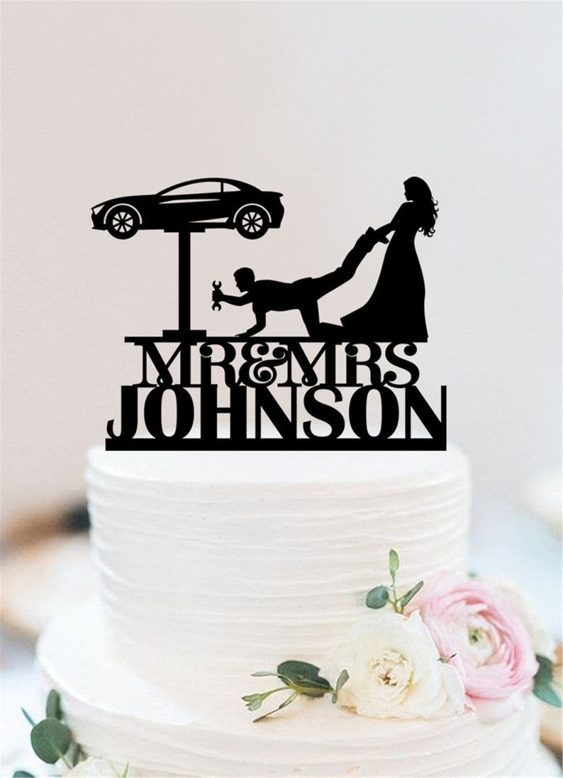 May include: Black silhouette cake topper of a bride pulling a groom who is working on a car on a lift. The text "MR & MRS JOHNSON" is below the figures.