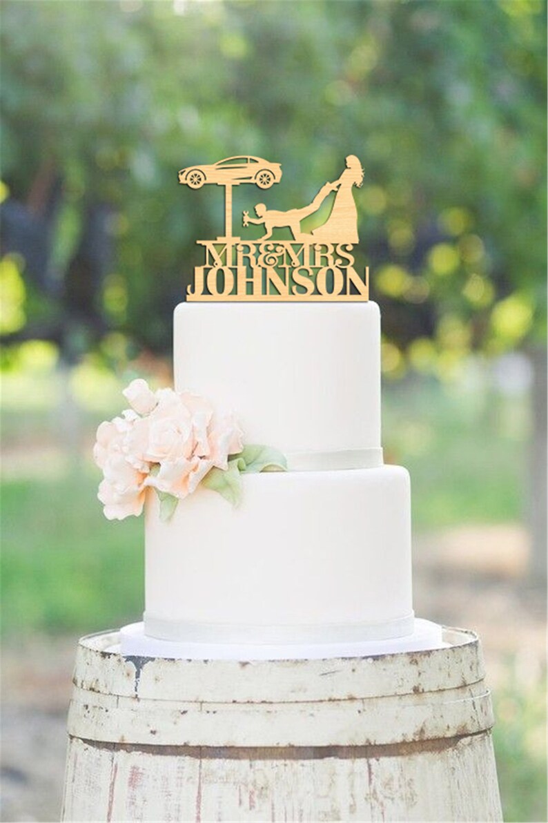 May include: A wooden wedding cake topper featuring a bride pulling a groom from under a car on a lift. The topper says "Mr. & Mrs. Johnson".