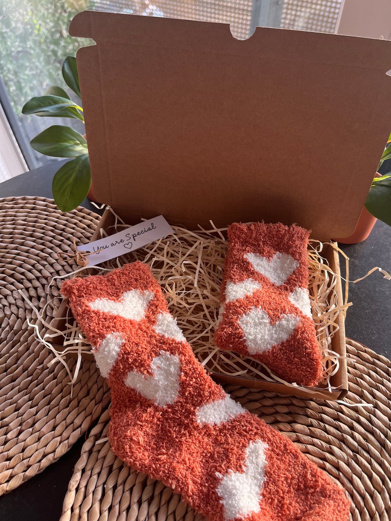 Pu&ograve; includere: Un paio di calzini morbidi con cuori bianchi su uno sfondo terracotta. I calzini sono confezionati in una scatola di cartone con carta triturata e un piccolo cartellino che dice "You are Special" con un cuore.