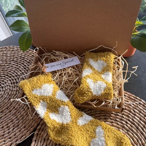 Pu&ograve; includere: Una scatola regalo piena di calzini gialli pelosi con cuori bianchi. La scatola &egrave; rivestita di carta triturata e include un'etichetta che dice "You are Special" con un cuore.