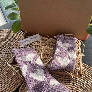 Pu&ograve; includere: Una scatola regalo piena di calzini morbidi con motivo a cuori viola e bianchi. La scatola &egrave; aperta e i calzini sono visibili. Un piccolo cartellino con il testo "You are Special" &egrave; attaccato alla scatola.