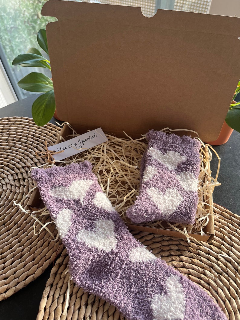Pu&ograve; includere: Una scatola regalo piena di calzini morbidi con motivo a cuori viola e bianchi. La scatola &egrave; aperta e i calzini sono visibili. Un piccolo cartellino con il testo "You are Special" &egrave; attaccato alla scatola.