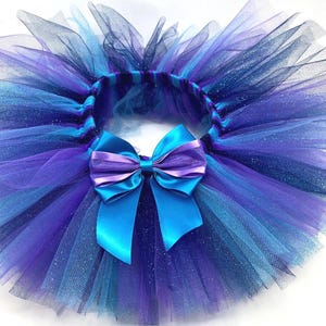 May include: A vibrant tutu skirt in shades of blue and purple, featuring layers of tulle. A large satin bow in turquoise and purple accents the front. The skirt is designed for children's wear.