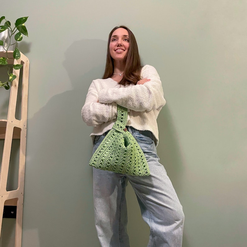 a woman leaning against a wall holding a green purse
