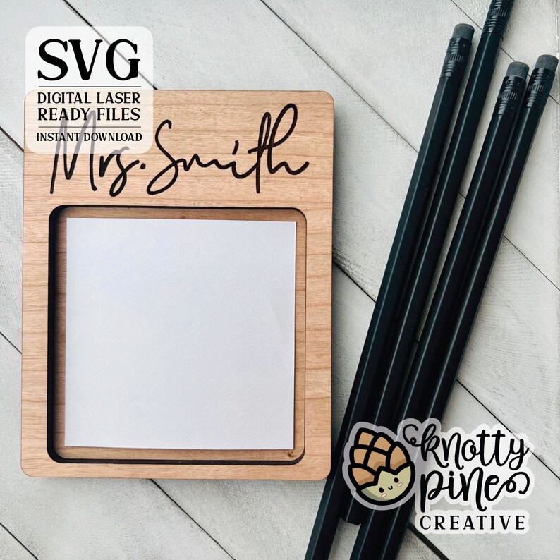 Pu&ograve; includere: Un organizzatore da scrivania in legno con un'apertura per un blocco note e un'iscrizione personalizzata che recita "Mrs. Smith". L'organizzatore &egrave; posto su una superficie in legno bianco con matite nere accanto. Un piccolo adesivo con un pigna di cartone animato e il testo "knotty pines creative" &egrave; visibile nell'angolo in basso a destra.