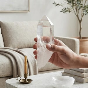 May include: A large, clear, hexagonal quartz crystal point with a pointed termination and a semi-translucent base. The crystal features natural internal inclusions and facets, displaying a transparent, glass-like appearance throughout its structure.