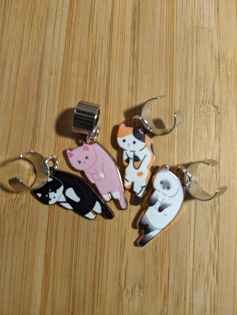 May include: Four cat-themed hair clips with silver metal clasps. The cats are depicted in various poses and colors, including black and white, pink, and orange and white.