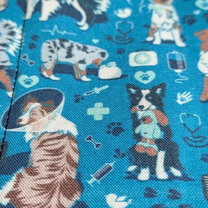 May include: Blue fabric with a repeating pattern of dogs, hearts, bones, and medical symbols. The dogs are in various poses and breeds, including a border collie, a husky, and a terrier.